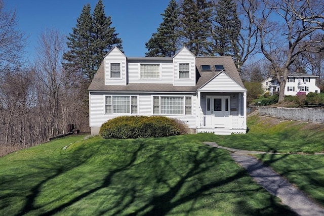new england style home featuring roof with shingles and a front lawn