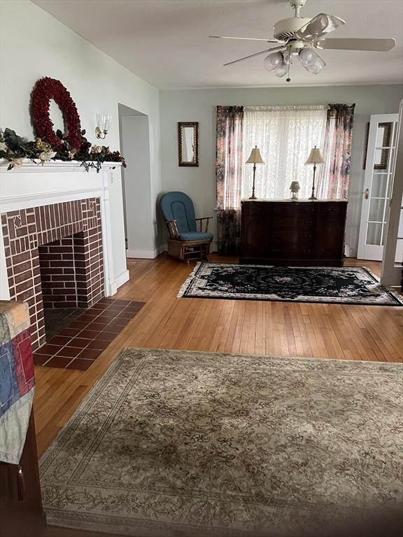 living room with wood-type flooring, baseboards, a ceiling fan, and a tiled fireplace