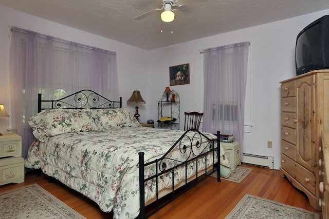 bedroom with a ceiling fan, wood finished floors, and a baseboard radiator