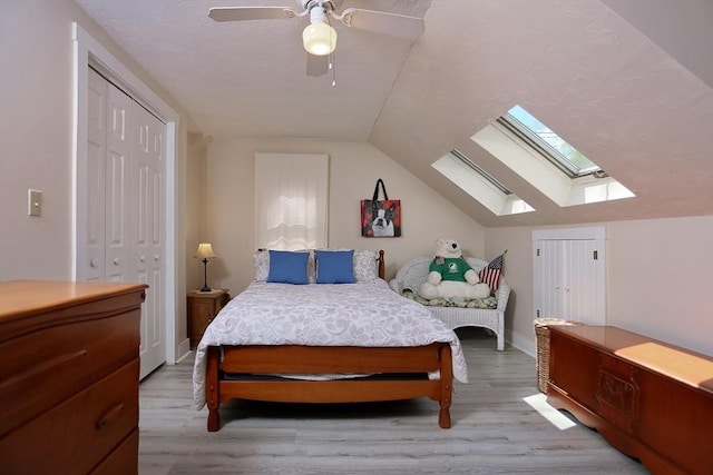 bedroom featuring a closet, light wood-style flooring, ceiling fan, and vaulted ceiling with skylight