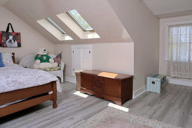 bedroom with lofted ceiling with skylight, baseboards, and wood finished floors