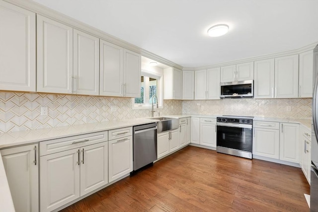 kitchen with wood finished floors, a sink, stainless steel appliances, light countertops, and white cabinetry