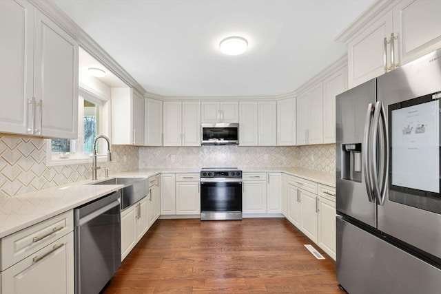 kitchen featuring decorative backsplash, appliances with stainless steel finishes, dark wood-style floors, white cabinetry, and a sink