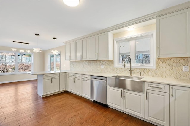 kitchen with dark wood-type flooring, a sink, a peninsula, light countertops, and dishwasher