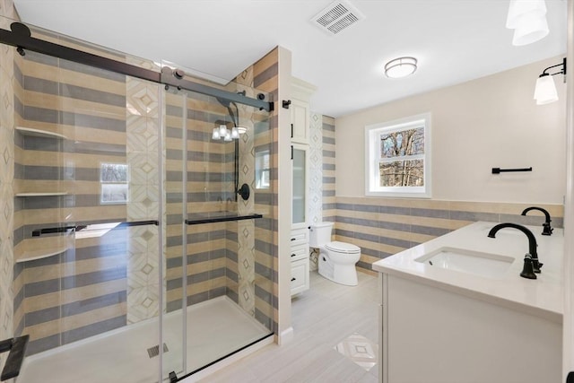 full bath featuring visible vents, a wainscoted wall, toilet, tile walls, and vanity