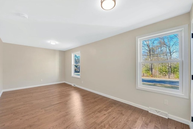 unfurnished room featuring wood finished floors, visible vents, and baseboards