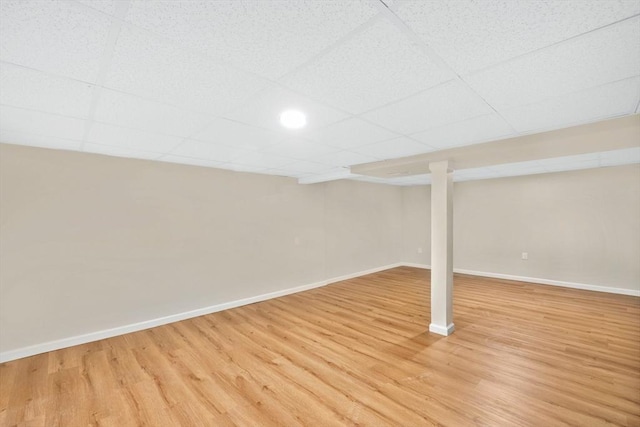 finished basement featuring a paneled ceiling, baseboards, and light wood-style floors