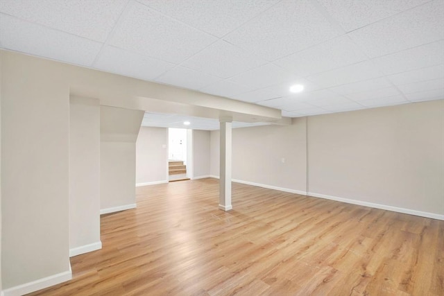 finished below grade area with light wood-style flooring, baseboards, and a drop ceiling