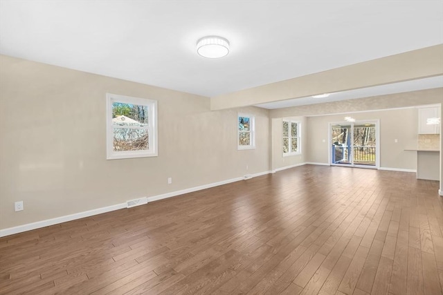 unfurnished living room with plenty of natural light, dark wood-type flooring, and baseboards