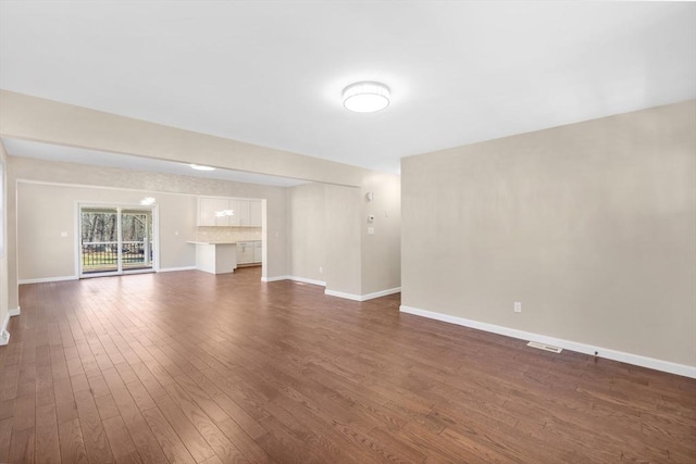 unfurnished living room with dark wood-type flooring, visible vents, and baseboards