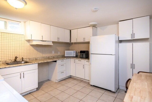 kitchen with tasteful backsplash, white appliances, light tile floors, sink, and white cabinetry