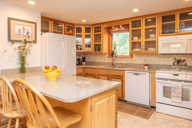 kitchen featuring tasteful backsplash, white appliances, a kitchen bar, light tile floors, and sink