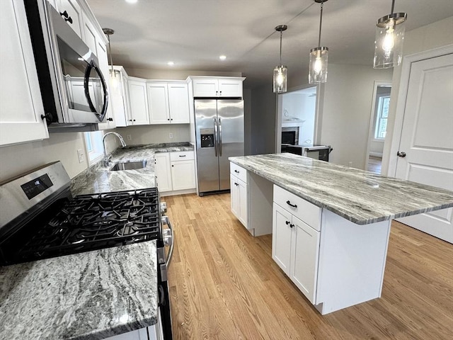 kitchen with sink, appliances with stainless steel finishes, hanging light fixtures, white cabinets, and a kitchen island