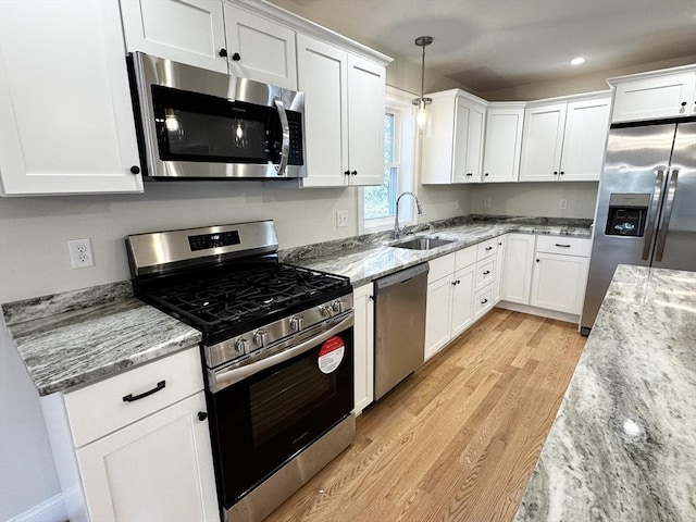 kitchen featuring appliances with stainless steel finishes, sink, white cabinets, light stone countertops, and light hardwood / wood-style flooring