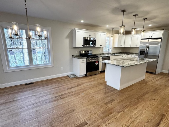 kitchen featuring appliances with stainless steel finishes, white cabinetry, hanging light fixtures, a kitchen island, and dark stone counters