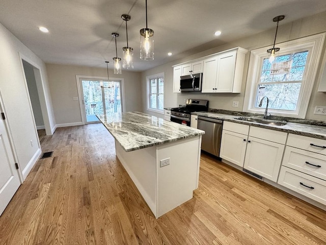 kitchen with decorative light fixtures, sink, white cabinets, a center island, and stainless steel appliances