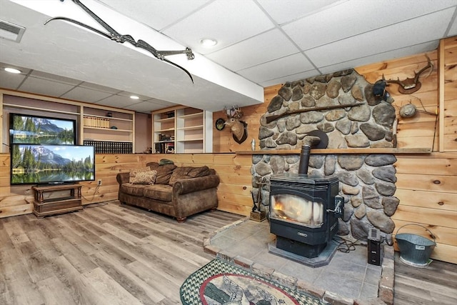 living room featuring a drop ceiling, wooden walls, hardwood / wood-style floors, and a wood stove