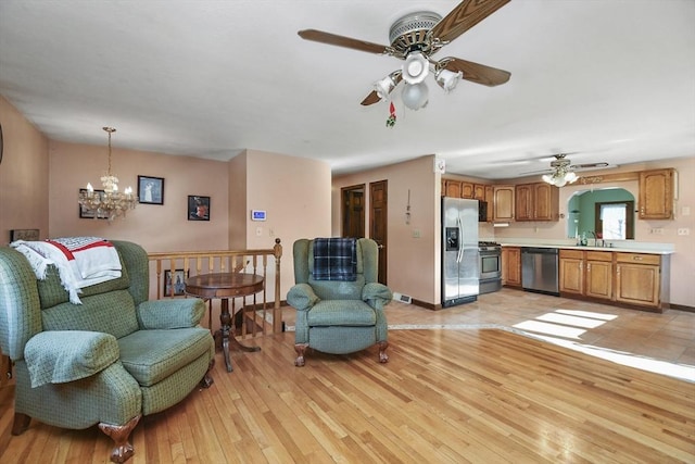 living room with sink, ceiling fan with notable chandelier, and light hardwood / wood-style flooring