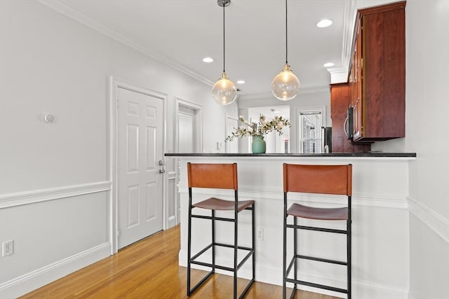 53 Woodward St Unit 2, Boston, MA 02127 - kitchen featuring a kitchen bar, hanging light fixtures, light wood-type flooring, dark countertops, and ornamental molding
