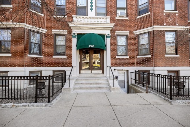 view of exterior entry with fence and brick siding