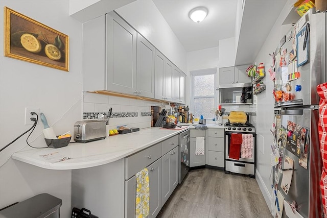 kitchen with light wood-style floors, appliances with stainless steel finishes, backsplash, and gray cabinetry