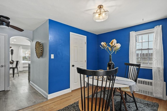 dining room with arched walkways, radiator, baseboards, and wood finished floors