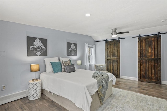 bedroom with ceiling fan, a barn door, wood finished floors, and baseboards