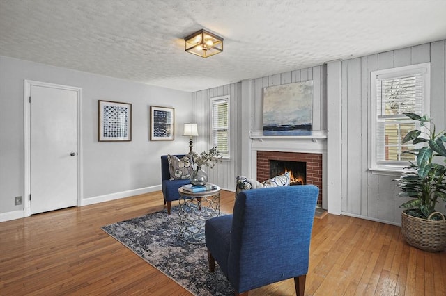 living area featuring a textured ceiling, a fireplace, baseboards, and hardwood / wood-style floors