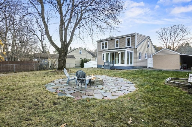 back of house featuring a sunroom, a fenced backyard, a lawn, and a fire pit