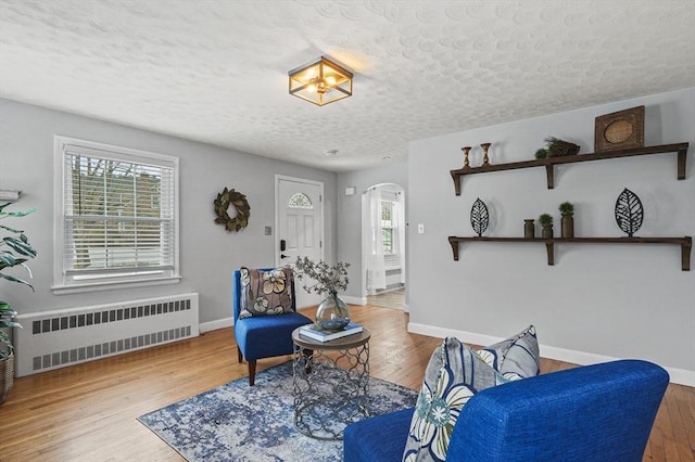 sitting room with baseboards, arched walkways, radiator heating unit, wood finished floors, and a textured ceiling