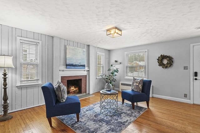 sitting room featuring a textured ceiling, baseboards, a brick fireplace, radiator heating unit, and wood-type flooring