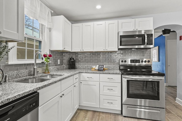 kitchen featuring stainless steel appliances, arched walkways, a sink, and light wood-style flooring