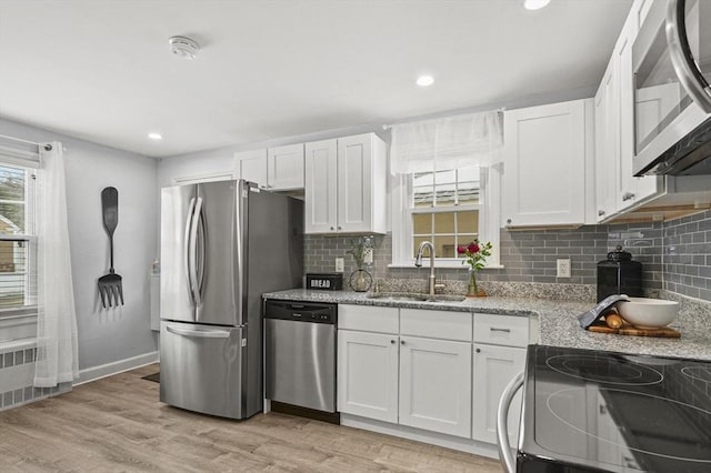 kitchen with stainless steel appliances, light wood-style floors, white cabinets, a sink, and light stone countertops