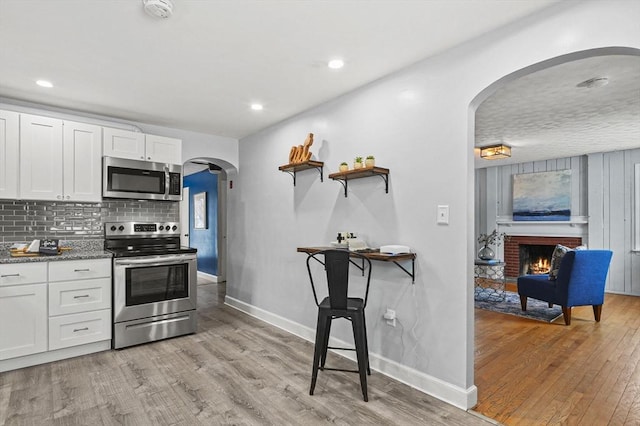 kitchen with light wood-style floors, a fireplace, arched walkways, and stainless steel appliances