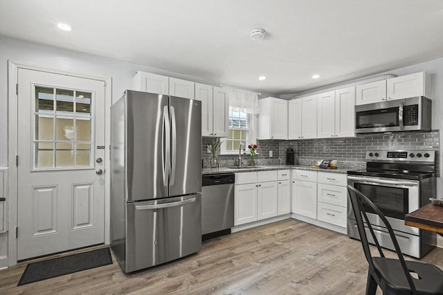 kitchen featuring light wood-style flooring, a sink, white cabinets, appliances with stainless steel finishes, and decorative backsplash