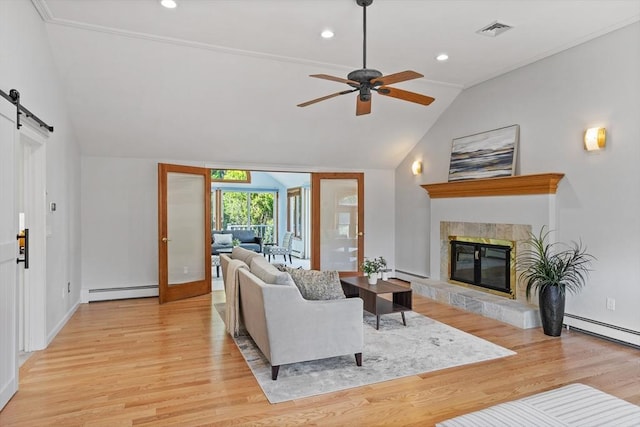 living room featuring vaulted ceiling, a baseboard heating unit, a ceiling fan, light wood-style floors, and a tiled fireplace