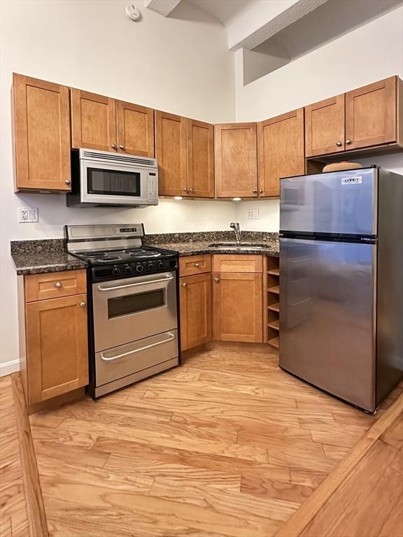 kitchen with appliances with stainless steel finishes, sink, dark stone counters, and a high ceiling