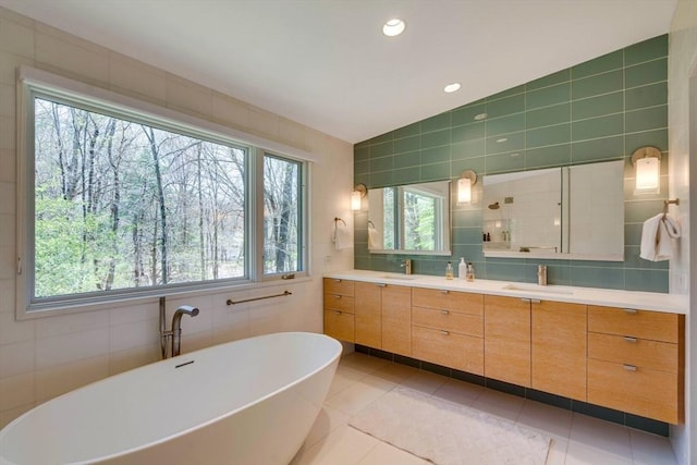 full bath featuring double vanity, a sink, a freestanding bath, and tile walls
