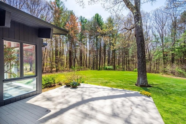 wooden terrace featuring a lawn and a wooded view