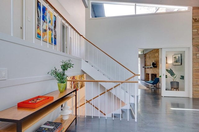 staircase with a stone fireplace, a towering ceiling, wood finished floors, and a healthy amount of sunlight