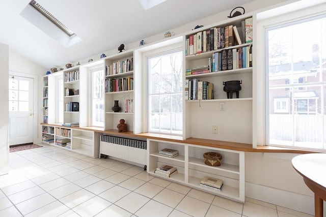 interior space featuring lofted ceiling with skylight, light tile patterned flooring, and radiator