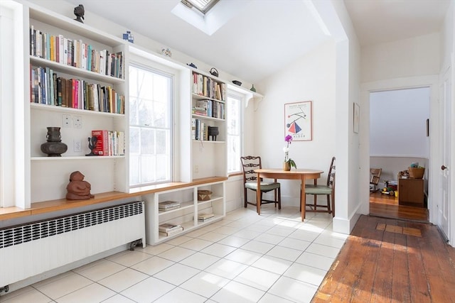 living area featuring radiator, lofted ceiling with skylight, and tile patterned flooring