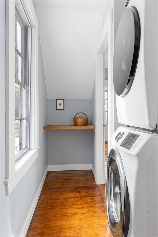 laundry room with stacked washer and dryer, wood finished floors, laundry area, and a healthy amount of sunlight