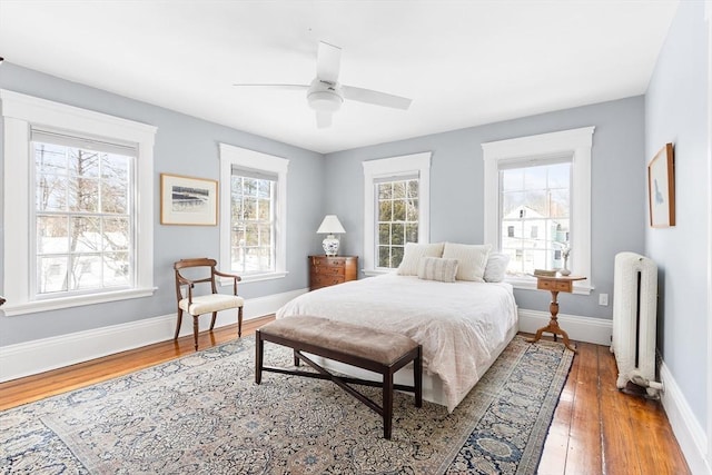 bedroom featuring baseboards, multiple windows, radiator heating unit, and hardwood / wood-style flooring