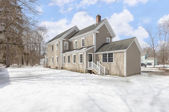 snow covered rear of property featuring a chimney