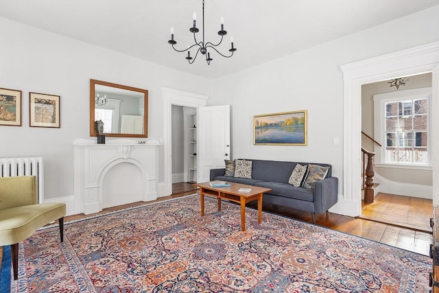 living area with wood finished floors, baseboards, stairway, radiator heating unit, and an inviting chandelier