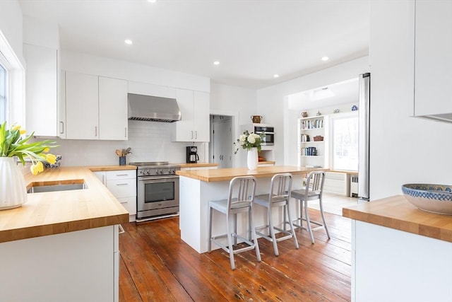 kitchen with appliances with stainless steel finishes, wood counters, white cabinetry, and range hood