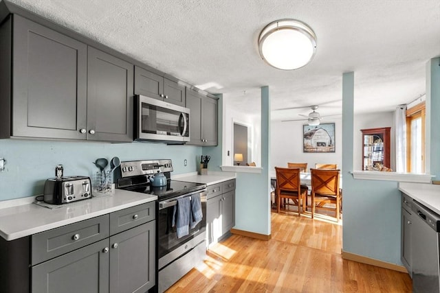 kitchen featuring ceiling fan, appliances with stainless steel finishes, light wood-type flooring, gray cabinets, and a textured ceiling