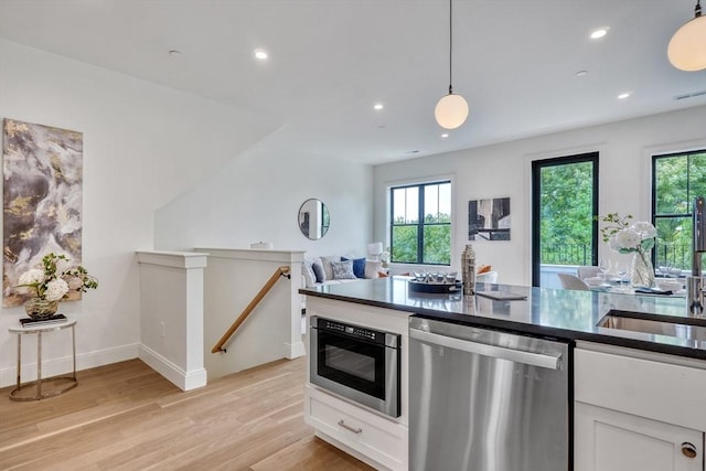 kitchen featuring built in microwave, dishwasher, light wood-type flooring, plenty of natural light, and white cabinetry