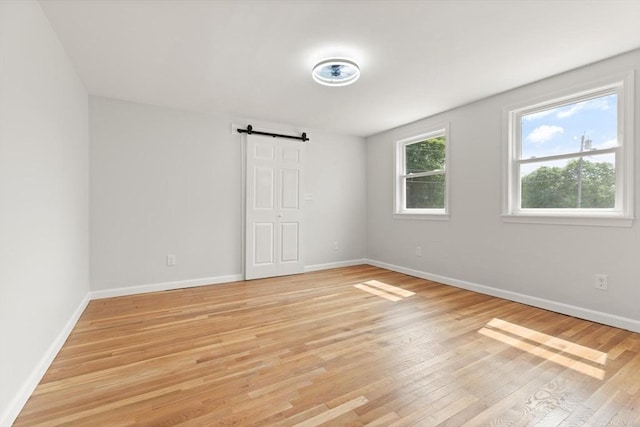 651 S Main St, Randolph, MA 02368 - unfurnished bedroom featuring a barn door, light wood-style flooring, and baseboards